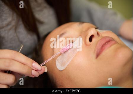 Primo piano di un estetista che applica estensioni ciglia alle ciglia di una donna in un salone di bellezza. Trattamento di bellezza professionale e cura di sé. Foto Stock