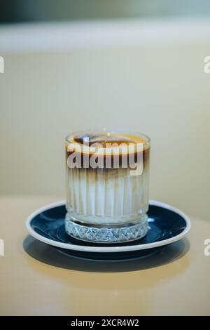 Un caffè a strati meticolosamente preparato si trova in un bicchiere trasparente, rivelando la sua stratificazione cremosa e ricca di espresso, servita su un piattino decorato Foto Stock