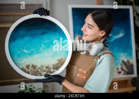 Donna artistica soddisfatta che guarda opere d'arte in resina epossidica fatte a mano realizzate in tecnica liquida. Foto Stock