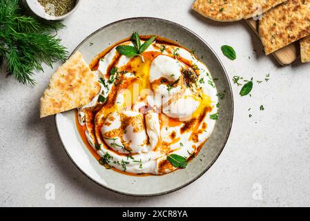 Uova turche Cilbir e pane pita fresco per la colazione tradizionale turca servita su piatto da vicino, vista dall'alto. Cucina turca, mezze. Uovo in camicia Foto Stock