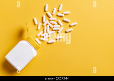 Capsule integratore bianche in flacone di plastica su sfondo giallo brillante, vista dall'alto, spazio di copia. Pillole medicinali, vitamina. Concetto di biohacking. Foto Stock