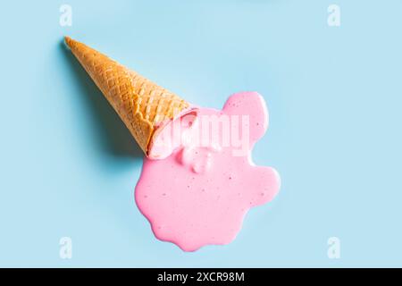 Cono per cialde gelato con gelato rosa fuso su sfondo blu pastello. Design minimalista e creativo del concetto di cibo estivo. Foto Stock