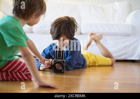 Due ragazzi, uno inginocchiato e l'altro steso per terra, si concentrano su una macchina fotografica d'epoca. La loro curiosità giocosa e il momento condiviso di creatività lo sono Foto Stock