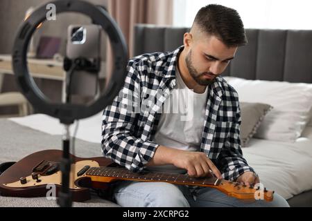 Music blogger che registra la lezione di chitarra con smartphone e lampada ad anello a casa Foto Stock