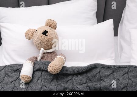 Simpatico orsacchiotto con bendatura e termometro sotto coperta nel letto Foto Stock