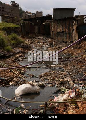 Un torrente pieno di rifiuti e rifiuti che attraversa la baraccopoli di Kibera a Nairobi, con tubi di approvvigionamento idrico che attraversano da un lato all'altro Foto Stock