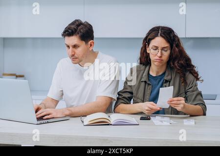 La coppia si siede a tavola, gestendo insieme le proprie finanze. L'uomo lavora su un portatile, mentre la donna, con un'espressione preoccupata, guarda la ricevuta. Foto Stock