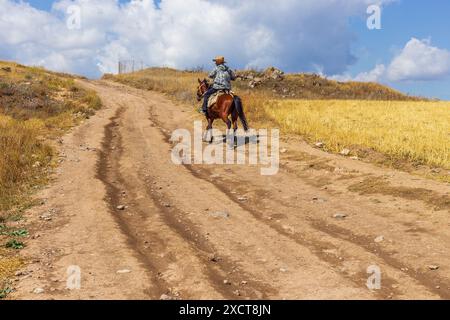 Sisian, Armenia - 3 settembre 2019: Un uomo che viaggia su un cavallo, strada di montagna ghiaia. Foto Stock