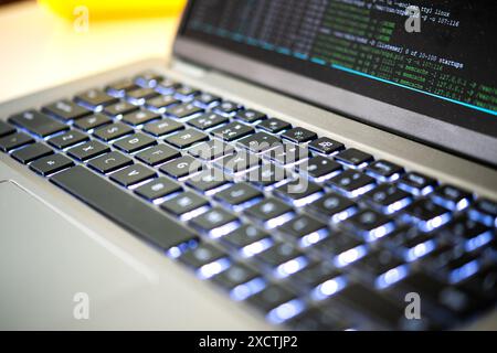 Acquisizione della tastiera illuminata di un notebook moderno, con codice di programmazione visibile sullo schermo, che enfatizza la tecnologia avanzata, l'hacking, il brach dei dati e gli attacchi ddos Foto Stock