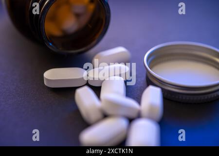 Primo piano di pillole bianche che fuoriescono dalla bottiglia di vetro scuro su sfondo blu moody, farmaci prescritti e crisi di oppioidi, farmaci darknet Foto Stock