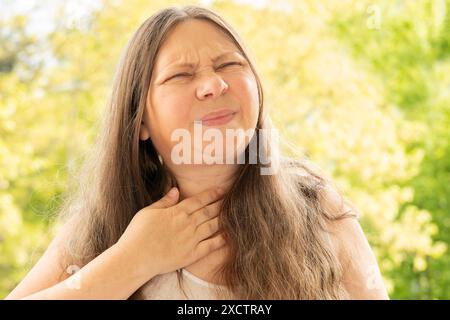 Primo piano collo femminile maturo, paziente che tiene in mano l'area interessata, sperimentando dolore alla gola, preoccupazione per la salute, perdita di voce, tonsillite Foto Stock