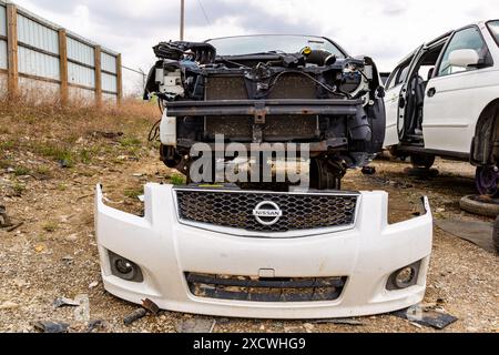 Il paraurti anteriore bianco di una Nissan Sentra si trova di fronte a un'auto spazzatura presso il cantiere LKQ Pick Your Part di Fort Wayne, Indiana, USA. Foto Stock