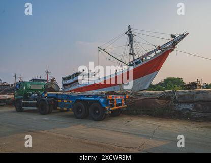 Giacarta, Indonesia - 9 maggio 2024. Una vista a contrasto tra il moderno grande camion affiancato e la tradizionale nave in legno a riposo nel porto di Sunda Kelapa. Foto Stock