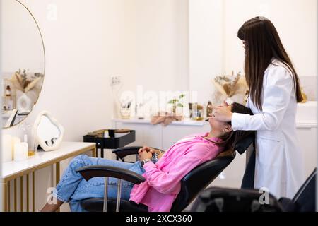 Estetista che fa un trattamento viso. Giovane donna latina rilassata in un salone di bellezza professionale con massaggio viso spa. Foto Stock