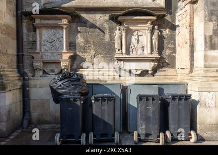 Vienna, Austria - 12 maggio 2024: Contenitori di rifiuti impilati contro le mura medievali della chiesa. Nessuna persona visibile Foto Stock