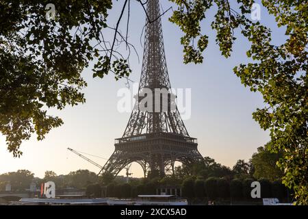 Parigi, Francia - 7 giugno 2024: Torre Eiffel alla luce del mattino presto incorniciata da foglie di alberi. Logo dei giochi olimpici montato sulla torre e gru da costruzione Foto Stock