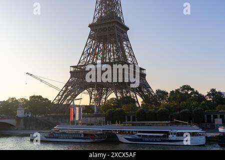 Parigi, Francia - 7 giugno 2024: Torre Eiffel alla luce del mattino presto incorniciata da foglie di alberi. Logo dei giochi olimpici montato sulla torre e gru da costruzione Foto Stock