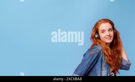 Donna con capelli rossi lunghi che indossa le cuffie su blu Foto Stock