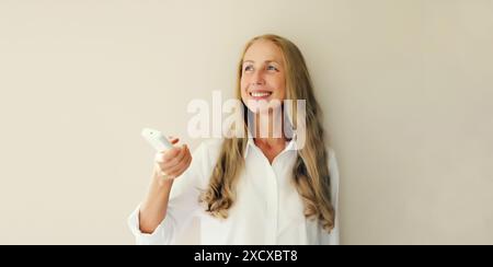 Felice sorridente donna caucasica di mezza età accende il condizionatore o la TV utilizzando il telecomando a casa Foto Stock