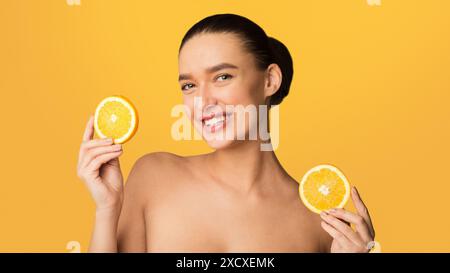 Donna con due fette di arancione su sfondo giallo Foto Stock