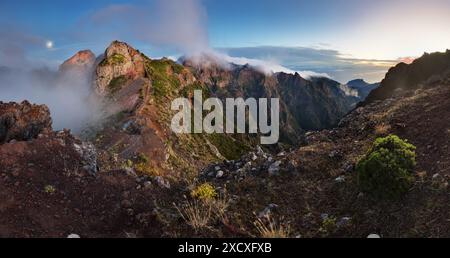 Paesaggio di alba in montagna sopra le nuvole nell'isola di Madeira su Pico do Arieiro su ripide scogliere e alte vette con la nebbia mattutina ancora coverin Foto Stock