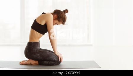 Donna seduta su Yoga Mat con le mani sulle ginocchia Foto Stock