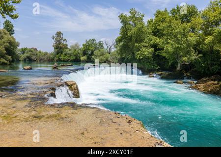 Le splendide acque blu della cascata Manavgat vicino alla città turca di Side vicino ad Antalya in Turchia in una giornata di sole con sole e alberi luminosi. Foto Stock