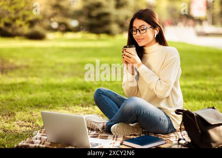 Donna che si gusta il caffè mentre usa il laptop a Park Foto Stock
