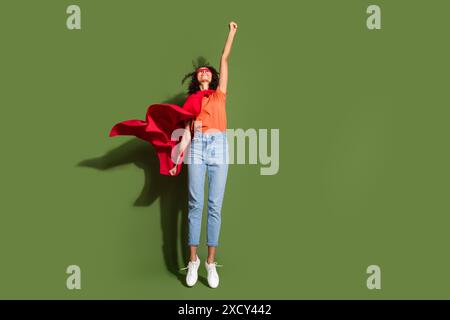 Foto a tutta lunghezza di una bella ragazza che vola supereroina vestita con elegante indumento arancione isolato su sfondo color cachi Foto Stock