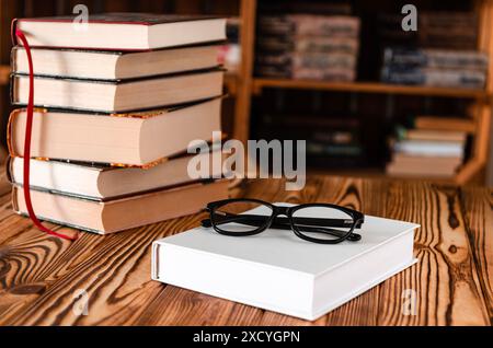 Occhiali neri adagiati su un libro bianco accanto a vecchi libri sullo sfondo di scaffali Foto Stock