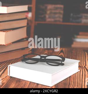 Occhiali neri adagiati su un libro bianco accanto a vecchi libri sullo sfondo di scaffali Foto Stock