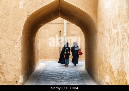 Yazd, Iran - 27 ottobre 2018: Donne iraniane che indossano un chador nero che camminano lungo le strette strade della storica città di Yazd. Foto Stock