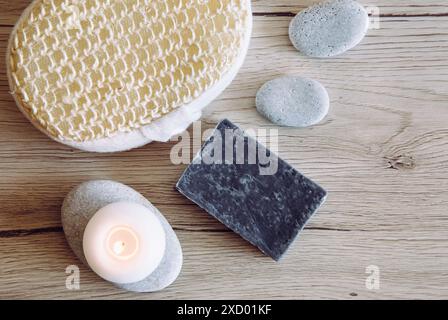 Vista piatta del sapone di argilla di colore grigio fatto a mano su sfondo in legno con candelabro e spugna da bagno, pietre marine piatte. Bagno di casa. Foto Stock