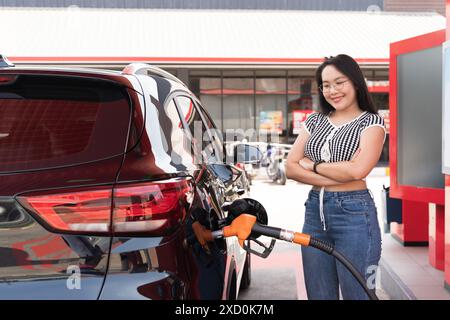 Una donna sta accanto a un'auto che viene riempita di gas. Indossa occhiali e una camicia a righe bianca e nera. BIO-Fuel presso Modern Petrol Stat Foto Stock