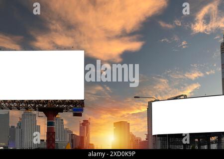 Due grandi cartelloni sono in primo piano sullo skyline della città. Il cielo è nuvoloso e il sole sta tramontando, creando un'atmosfera soffusa Foto Stock