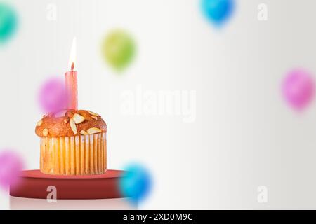 Palloncini colorati con candele accese sopra il cupcake di compleanno sul palco rosso su sfondo bianco per festeggiare il compleanno. Copia spazio. Foto Stock