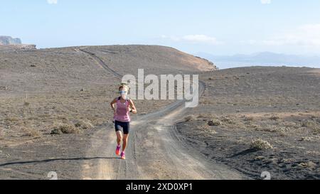 Una donna in abbigliamento atletico che corre su una pista sterrata in un arido paesaggio desertico sotto un cielo limpido. Foto Stock