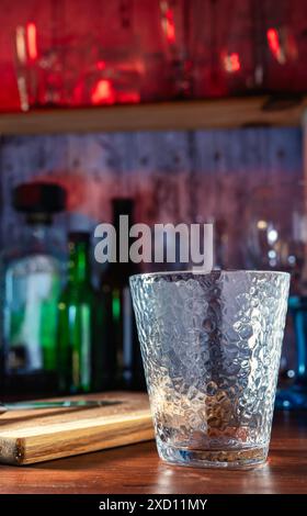 Vetro nel bar di un bar, sullo sfondo bicchieri e bottiglie con luci colorate. Cocktail, rum, vodka, atmosfera notturna, festa e freschezza. Jo Foto Stock