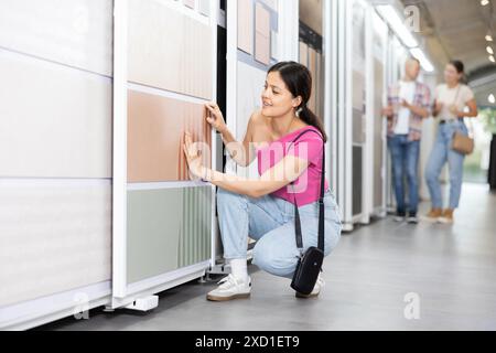 Donna asiatica che esamina campioni di piastrelle su espositore scorrevole in negozio Foto Stock