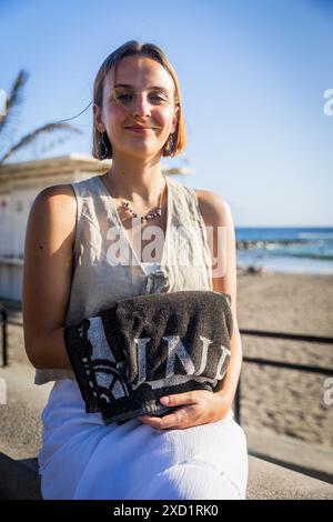 Una donna è seduta su una sporgenza vicino alla spiaggia con un asciugamano in mano, foto verticale. Foto Stock