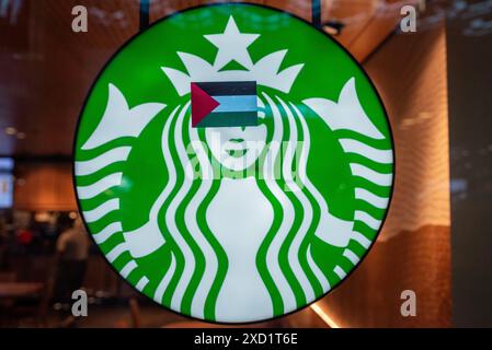 L'Aia, Olanda meridionale, Paesi Bassi. 19 giugno 2024. Un dimostratore filo-palestinese ha messo un adesivo Flag of Palestine sul logo del caffè Starbucks nella stazione centrale dell'Aia. Il 19 giugno 2024, i manifestanti filo-palestinesi protestarono davanti alla Tweede Kamer der Staten-Generaal (camera dei rappresentanti olandese). La polizia olandese e la Royal Marechausse (polizia militare reale) intervennero. (Credit Image: © James Petermeier/ZUMA Press Wire) SOLO PER USO EDITORIALE! Non per USO commerciale! Crediti: ZUMA Press, Inc./Alamy Live News Foto Stock