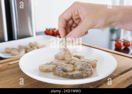 Una mano che raccoglie un pezzo di gambero crudo marinato da un piatto, pronto per essere spietato. Ricetta rapida per i gamberi di pesce Foto Stock