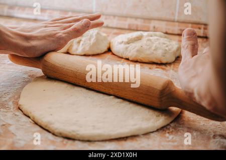 Stendere l'impasto con un mattarello di legno. Due palline di impasto sono sullo sfondo su una superficie infarinata. Foto Stock