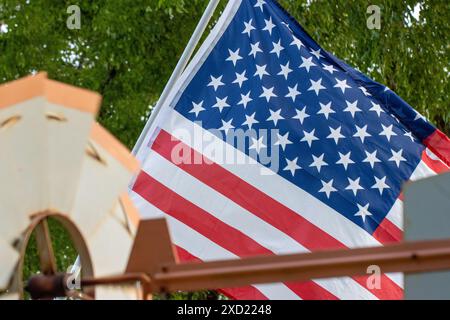 Vista della bandiera americana dietro un mulino a vento in metallo rustico sotto il fogliame degli alberi. Foto Stock