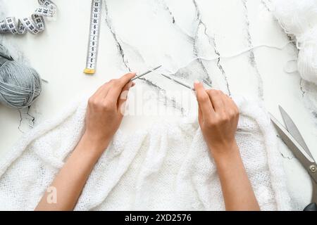 Donna che lavora a maglia con palle e aghi in filato su sfondo grunge bianco Foto Stock