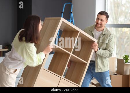 Felice giovane coppia che trasporta un ripiano in camera il giorno del trasloco Foto Stock