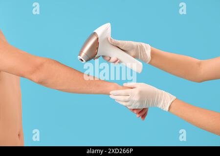 Cosmetologo che utilizza il fotoepilatore per rimuovere i peli dal corpo dell'uomo su sfondo blu Foto Stock