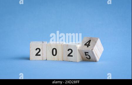 Dal 2024 al 2025, numeri su blocchi di legno. Su sfondo blu, concetto di anno nuovo. Foto Stock
