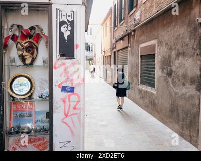 Solitario turista passeggiando attraverso un pittoresco vicolo di venezia, passando davanti all'antica architettura e a un tradizionale negozio di maschere Foto Stock