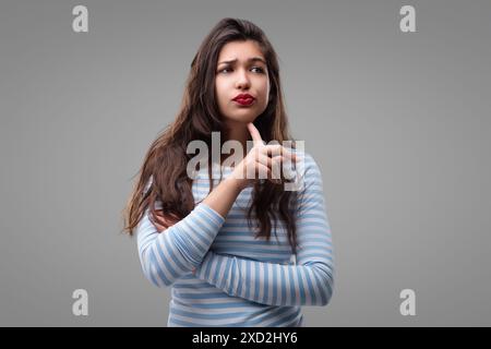 La giovane donna ha un aspetto premuroso, tiene il mento, contemplando una decisione. Sembra seria, preoccupata e un po' preoccupata, brainstorming con una h Foto Stock